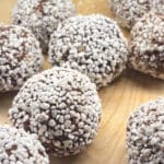 Chokladbollar rullade i kokosflingor på en träyta.