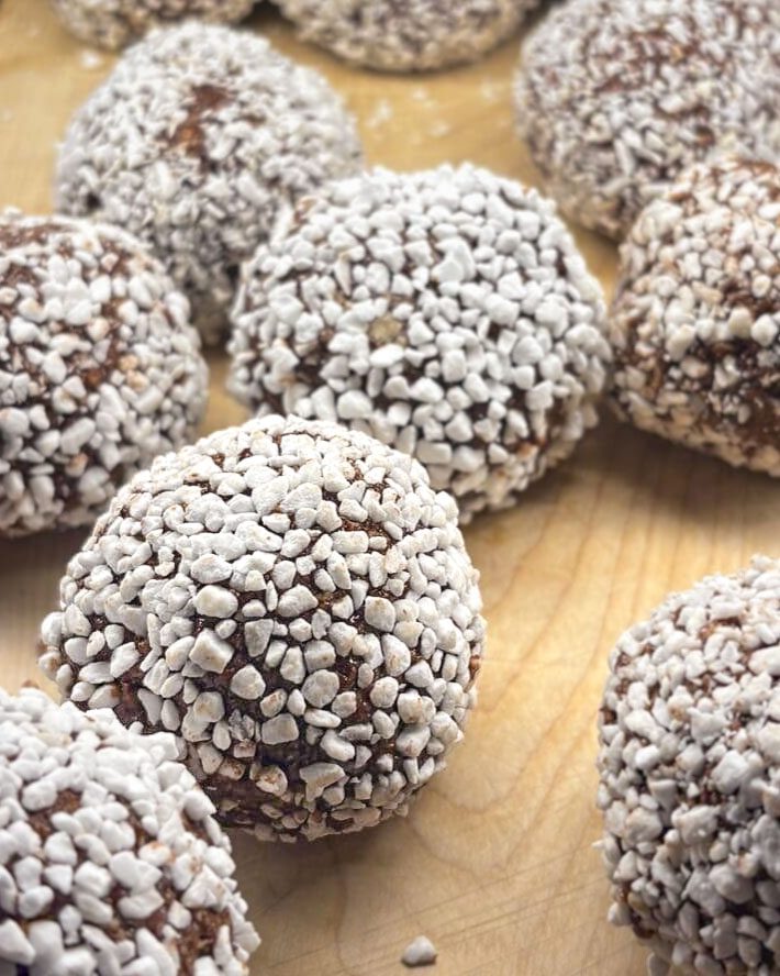 Chokladbollar med kokos och dadlar 9 Chokladbollar rullade i kokosflingor på en träyta.
