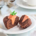 Chokladmuffins med orange frosting och en grön morotsdekoration på toppen, delad på en tallrik.