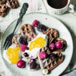 Tallrik med chokladvåfflor dekorerade med bär och grädde, samt en kopp kaffe vid sidan.