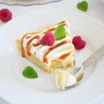 En bit citronkladdkaka med mascarponefrosting, dekorerad med hallon och mynta på en vit tallrik.