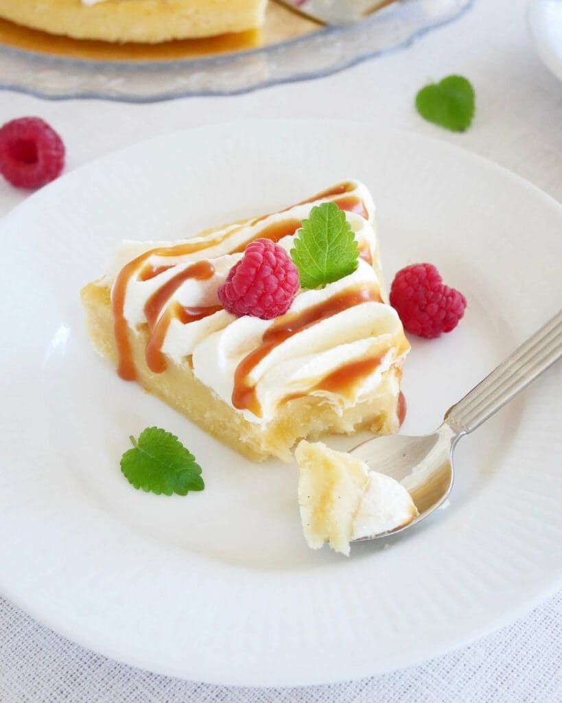 Jordgubbskladdkaka med smuldeg 7 En bit citronkladdkaka med mascarponefrosting, dekorerad med hallon och mynta på en vit tallrik.