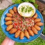 En tallrik med falafel, hummus och tomatsallad arrangerad på en blå tallrik.
