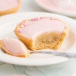 En glutenfri mazarin med rosa glasyr och små dekorationer på en tallrik, med en bit tagen.