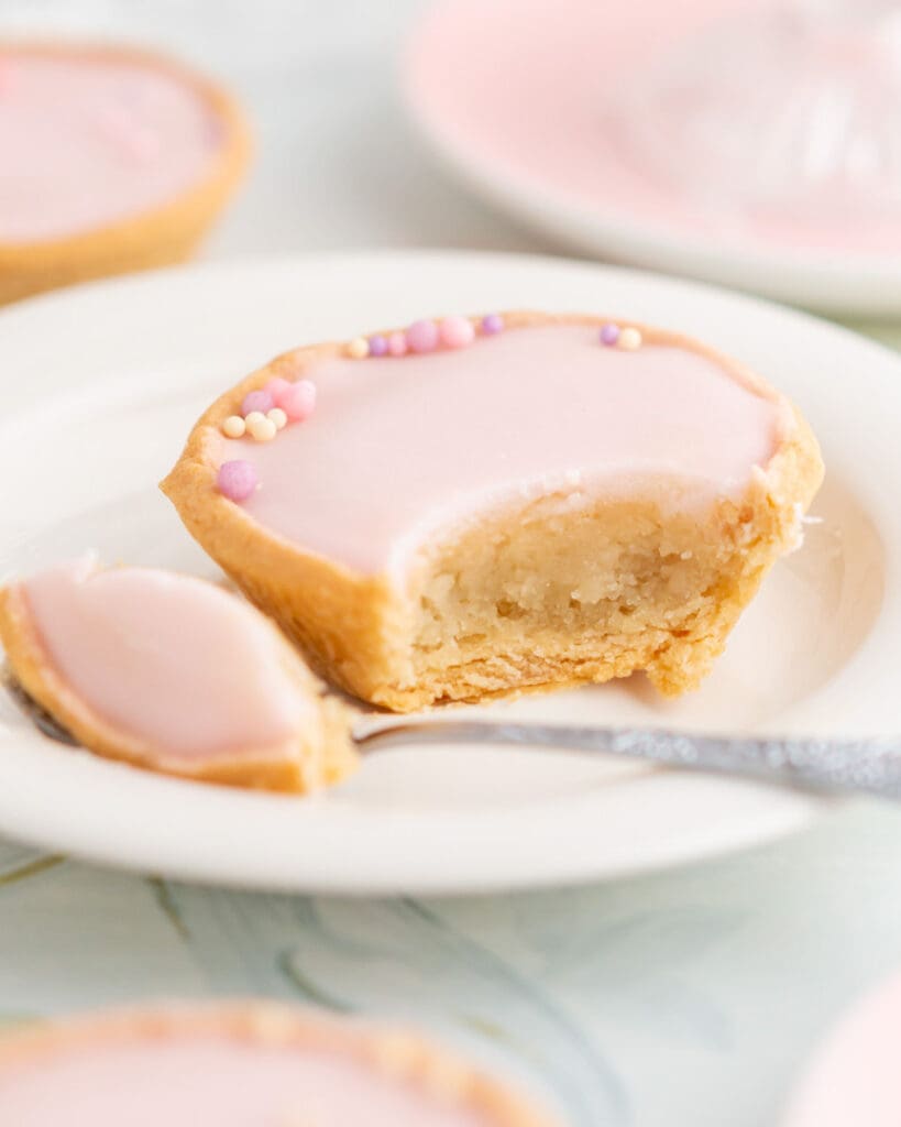 Chokladbollar med kokos och dadlar 10 En glutenfri mazarin med rosa glasyr och små dekorationer på en tallrik, med en bit tagen.