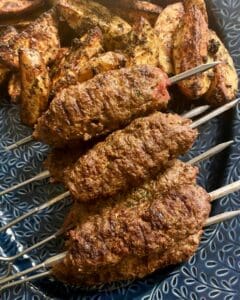 Tre grillade shish kebabspett placerade på en tallrik med ugnsbakade potatisar.