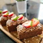Tre bitar chokladkaka med grädde, jordgubbar och kokosflingor på en träskärbräda.