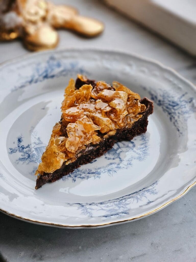 Kladdkaka med choklad och jordgubbsganache 8 En bit kladdkaka med cornflakes på en vit och blå mönstrad tallrik.