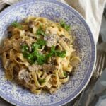 Tallrik med pasta, lövbiff, rostad vitlök och persilja på en blå och vit mönstrad tallrik.