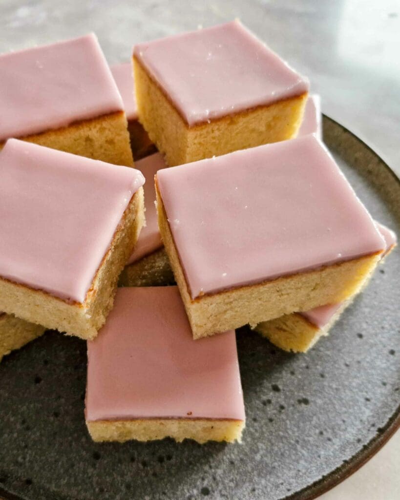 Mjuk mazarinkaka med vispad vaniljpannacotta 7 En tallrik med mazarinrutor täckta med rosa glasyr, staplade på varandra.