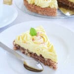 En bit av norsk succétårta med gul gräddfrosting och dekorationer på en tallrik.