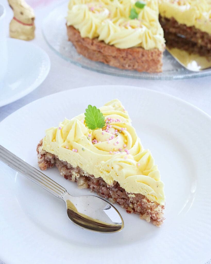 Moussetårta med hallon och passionsfrukt 11 En bit av norsk succétårta med gul gräddfrosting och dekorationer på en tallrik.