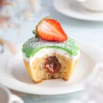 Muffin med grön glasyr, grädde och en skiva jordgubbe på toppen.