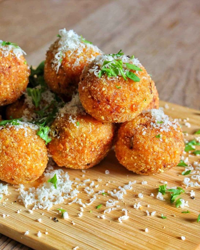 Pinsa 7 En hög av gyllenbruna arancini bollar med riven ost och grönsaker på en skärbräda.
