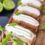 Skivor av blåbärskaka med lime och färskosttopping på en träplatta.