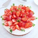 Cheesecake toppad med färska jordgubbar och grädde på en genomskinlig tårtfat.