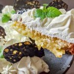 En bit citronkladdkaka med grädde och lakritschips på en tallrik.