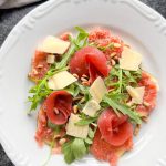 Tallrik med fikon carpaccio, ruccola, skivor av parmesan och pinjenötter.