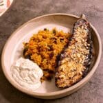 Rostad aubergine serverad med kryddat ris och vit sås i en skål.