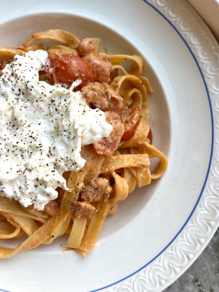 Öppen lasagne med burrata 13 En tallrik med pasta, körsbärstomater och burrata, toppad med svartpeppar.
