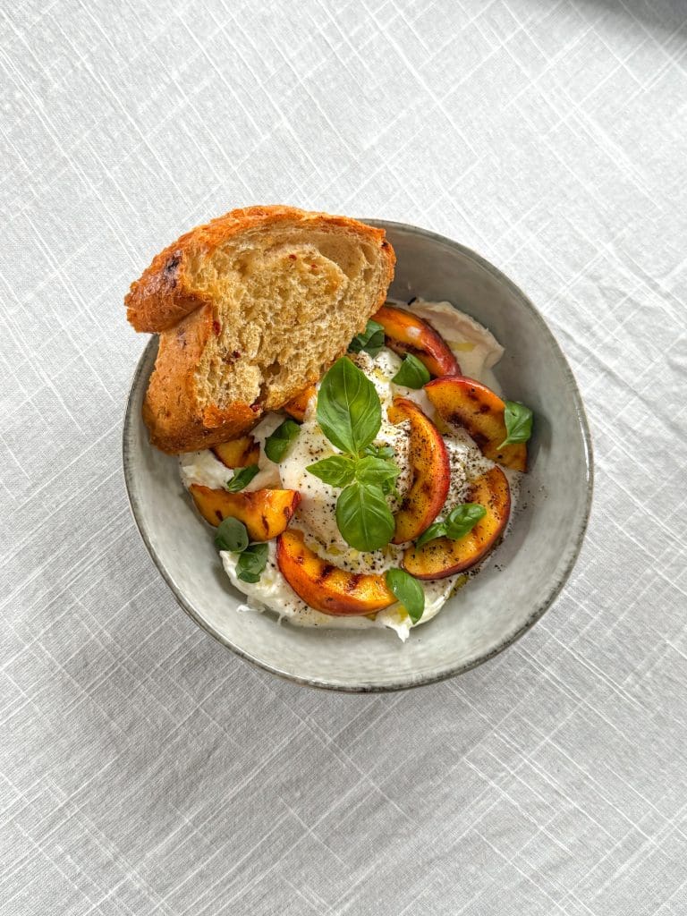 Burrata med persika, mynta och pinjenötter 10 En skål med skivor av nektariner, färsk basilika och en bit bröd på kanten.