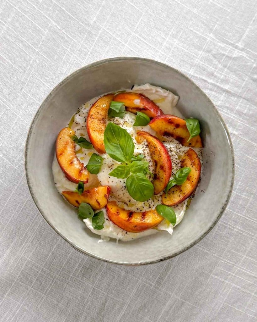 Cashew crunch sallad 9 Skål med mozzarella, grillade nektariner och färsk basilika på en ljus bakgrund.