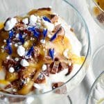 En dessert i en glasskål med grädde, chokladbitar och dekorationer av blommor.