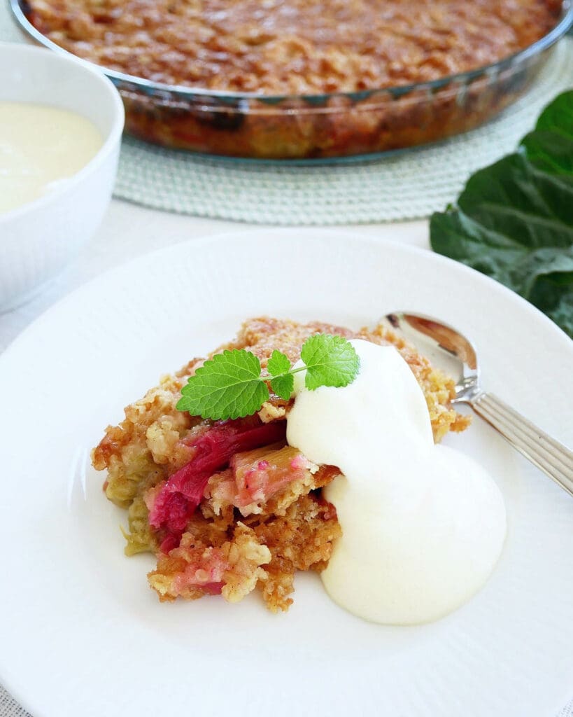 Citronmarängpaj 10 En bit rabarberpaj serverad med grädde på en vit tallrik.