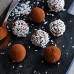 Chokladbollar rullade i kokos och kakao på en svart platta med en sked.