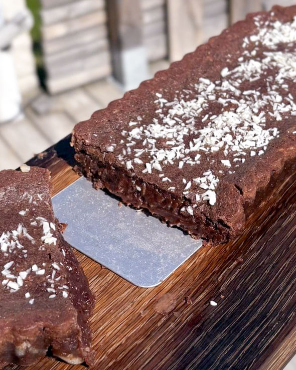 Chokladbollstårta med jordgubbsmousse 13 En skiva chokladbollskladdkaka med kokosflingor på toppen, skuren på en träskärbräda.