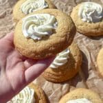 En hand som håller en kaka med gräddfrosting på toppen, omgiven av flera andra kakor.