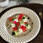 En tallrik med vattenmelonsallad som innehåller fetaost, mynta och blommor.