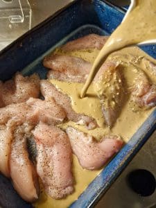 Kycklingfiléer i en ugnsform täckta med ädelostsås som hälls över dem.