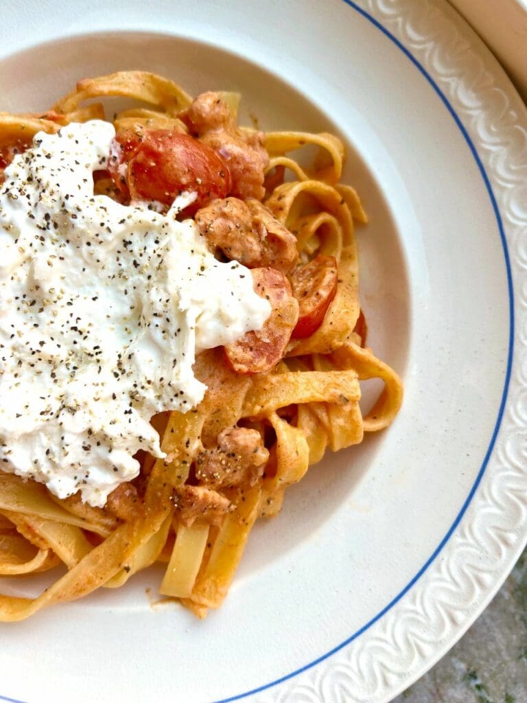 Tomatsås med soltorkad tomat och riven fetaost 10 Tallrik med pasta, salsicca, tomater och en klick gräddfil på toppen.