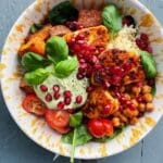 En skål med halloumi, grönsaker, bönor och granatäpplekärnor på en mönstrad tallrik.