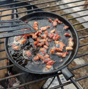 Gjutjärnspanna med stekt bacon som fräser på en grill.