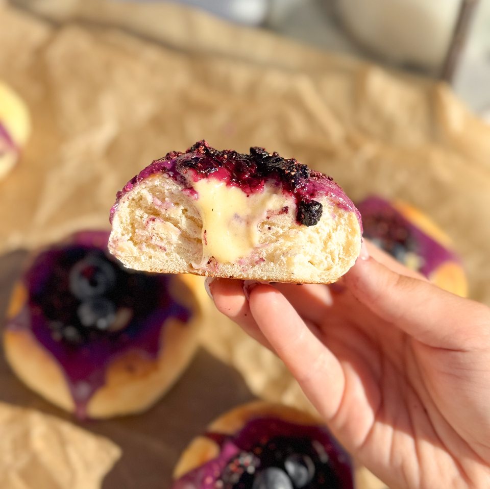 Mandas blåbärsbullar 6 En hand håller en bulle med blåbär och krämfyllning, delad på mitten för att visa insidan.