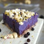 En bit no-bake blåbärscheesecake med nötter på toppen, placerad på en skärbräda.
