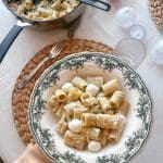 Tallrik med pasta, pesto och mozzarella bollar, serverad med en kastrull i bakgrunden.