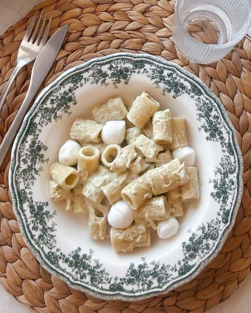 Krämig salsicciapasta med smak av citron och timjan 11 Tallrik med pasta, pesto och mozzarella bollar på en vävd underlägg.