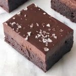 En bit brownie med chokladglasyr och havssalt på toppen, placerad på en ljus yta.