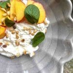 En skål med burrata, skivor av persika, pinjenötter och myntablad.