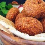 En skål med falafelbollar och pita bröd, dekorerad med mynta och grönsaker.