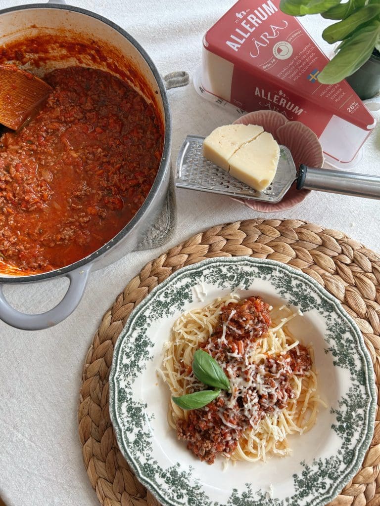 Lisas enkla köttbullar 8 Tallrik med spaghetti toppad med köttfärssås och riven parmesan, med basilika som dekoration.