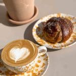 En kopp kaffe med hjärtformad lattekonst och en kardemummabulle på en tallrik.