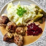 En tallrik med köttbullar, potatismos, sås, lingonsylt och inlagda gurkor.