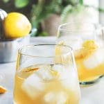 Två glas med Amaretto Sour-cocktail, is och citronskivor, på ett bord.