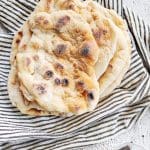 En hög med hembakat naanbröd på en randig kökshandduk.