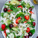 En färgglad sommarsallad med chèvre, gurka, tomater, avokado och nötter på ett vitt fat.