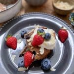 En skiva bananpannkaka dekorerad med grädde, blåbär och jordgubbar på en tallrik.